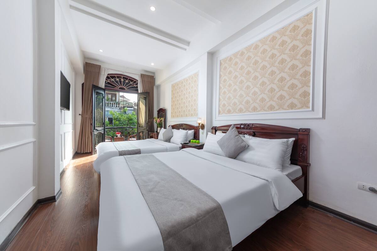 A hotel room with two beds, a large window, and a balcony view.
