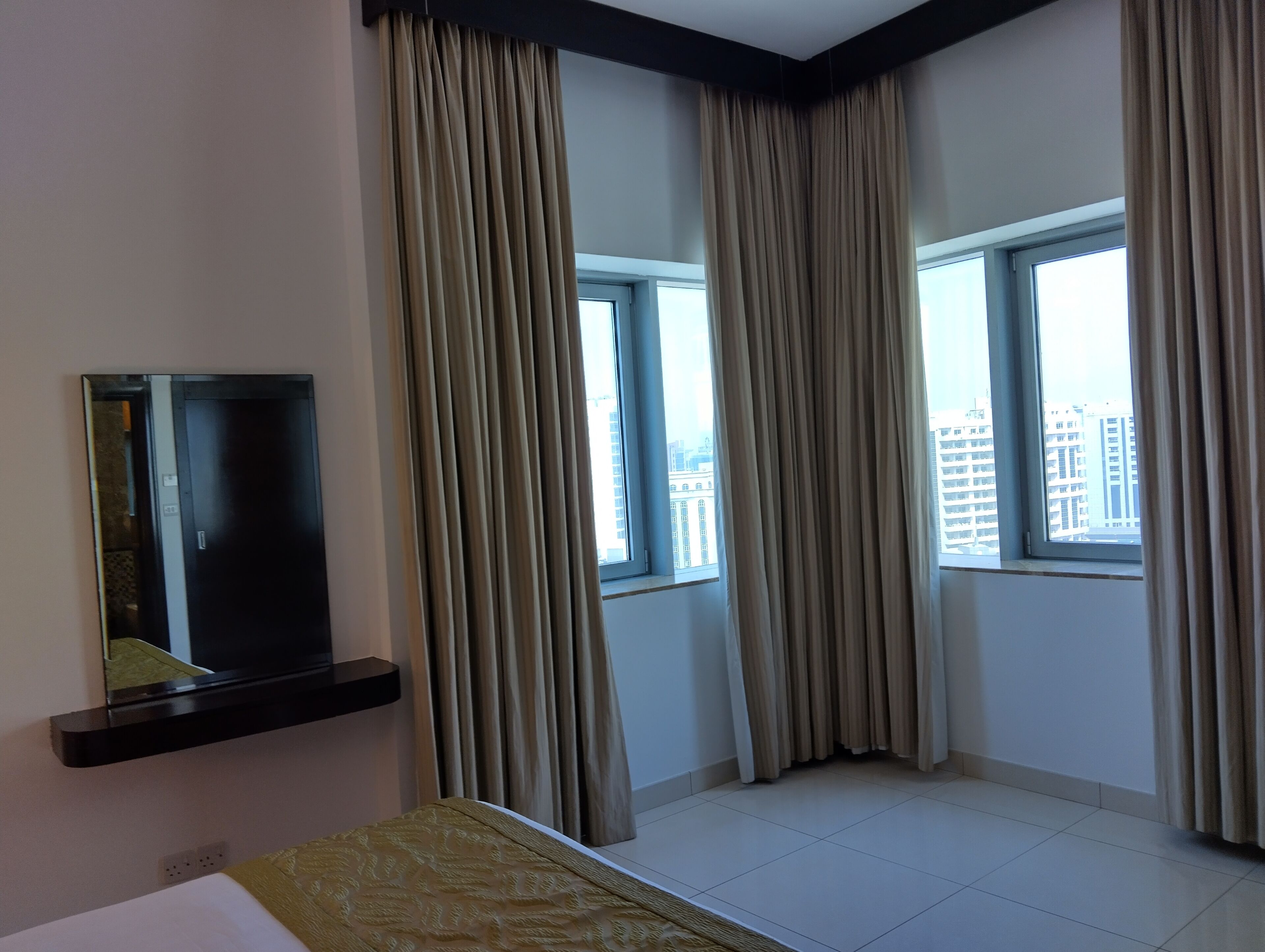 Una habitación de hotel con una cama, un televisor montado en la pared y ventanas amplias con cortinas.
