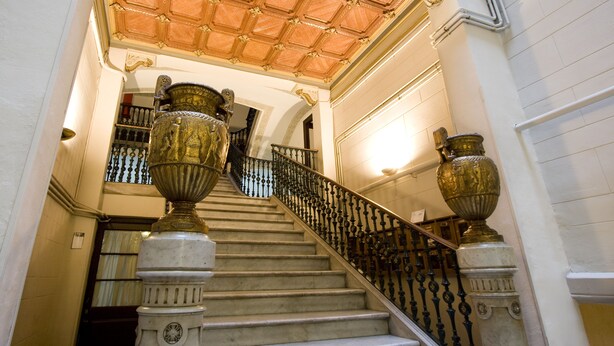 A grand staircase with ornate balustrades and large decorative urns at the base. - Palace Guesthouse (Barcelona)