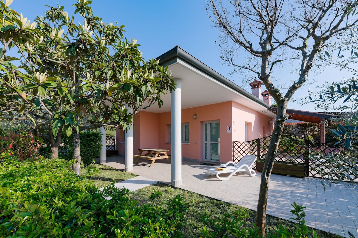 A pink building with a covered patio, a wooden table, and two white lounge chairs.