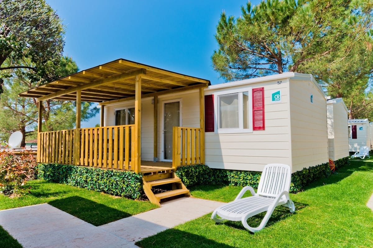 A mobile home with a wooden porch and a covered outdoor seating area.