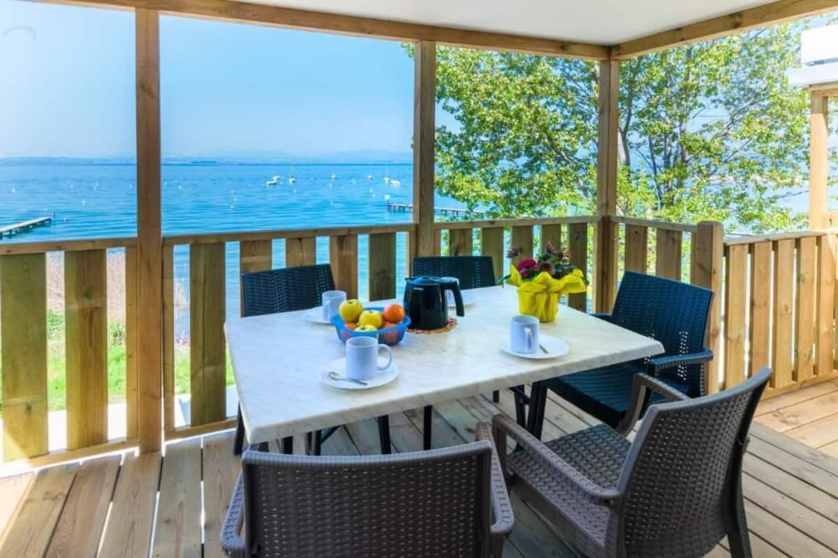 A wooden deck with a table and chairs, overlooking a body of water with boats.