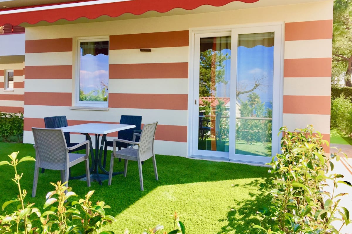 A house with a striped exterior, a covered patio with a table and chairs, and a well-maintained lawn.