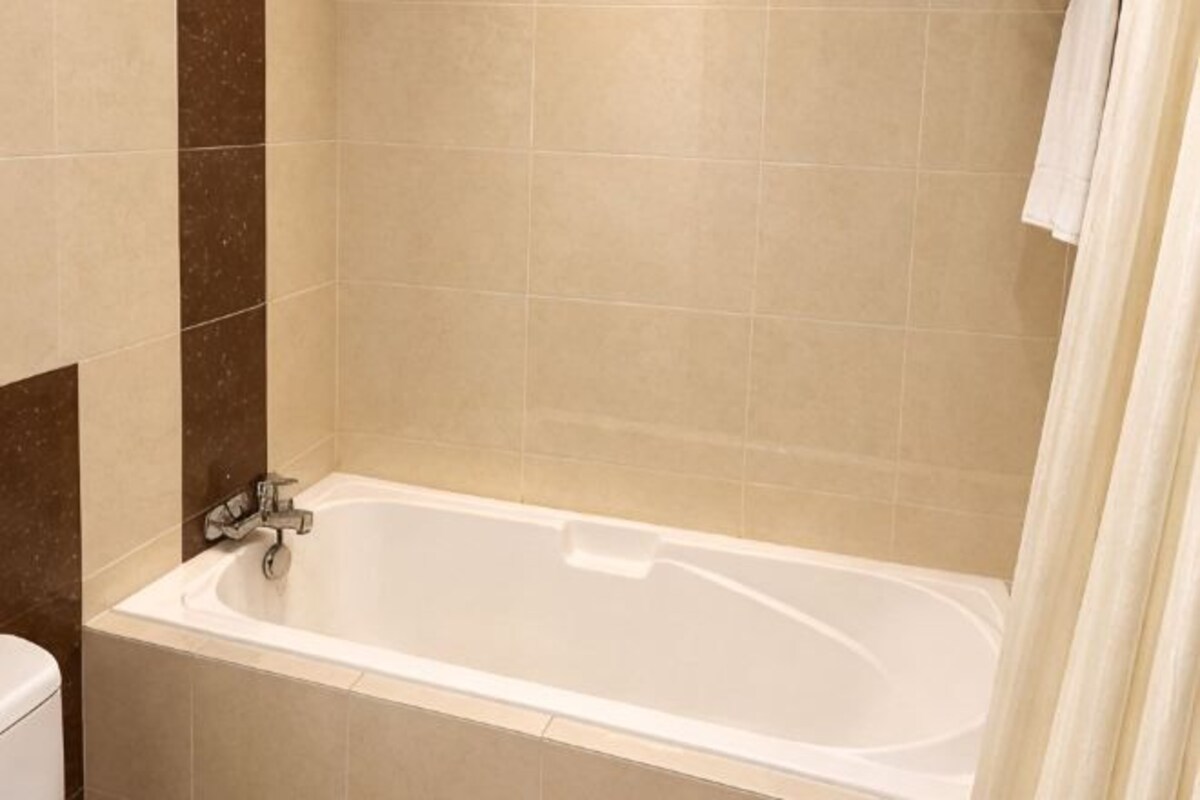 Eine Standardbadewanne in einem Badezimmer mit beigen Fliesen und einem weißen Vorhang.