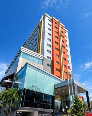 A multi-story hotel with a modern glass facade, a prominent red and white color scheme, and a flagpole. - Grand Antares Hotel (Medan)