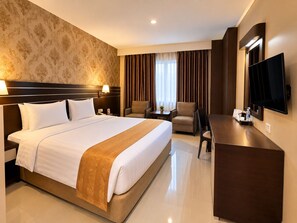 A hotel room with a large bed, a desk, a chair, a television, and a window with curtains. - Grand Antares Hotel (Medan)