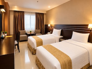 A hotel room with two beds, a desk, a chair, a nightstand, and a lamp. - Grand Antares Hotel (Medan)