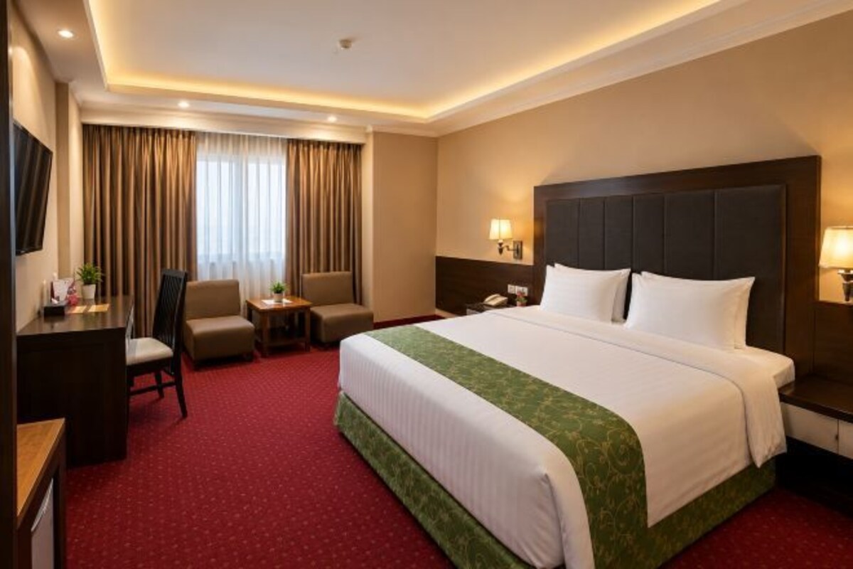 A hotel room with a large bed, a desk, two chairs, a small table, and a TV.