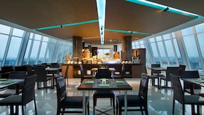 A modern restaurant with high ceilings, large windows, and a central bar area.