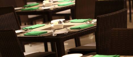 Un restaurante con varias mesas dispuestas, con servilletas verdes, platos blancos y cubiertos.