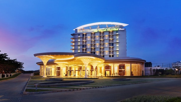 A modern hotel with a curved facade, a prominent entrance with illuminated canopy structures, and a clear view of the sky.