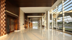 A modern hotel lobby with a reflective marble floor, wooden paneling, and large windows offering views of the outdoors.
