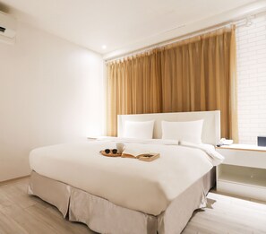 Una habitación de hotel con una cama grande, una mesita de noche con teléfono y una ventana con cortinas.