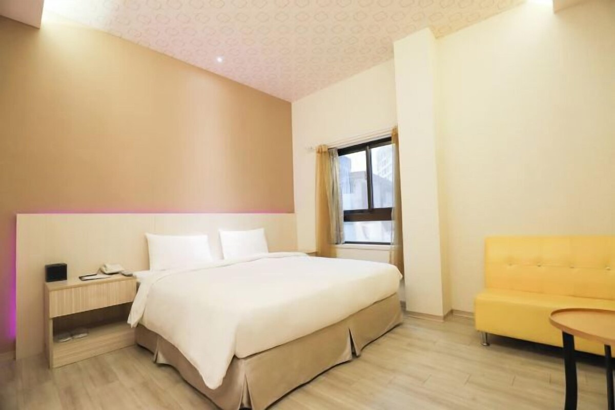 Una habitación de hotel con cama, mesita de noche y sofá amarillo.