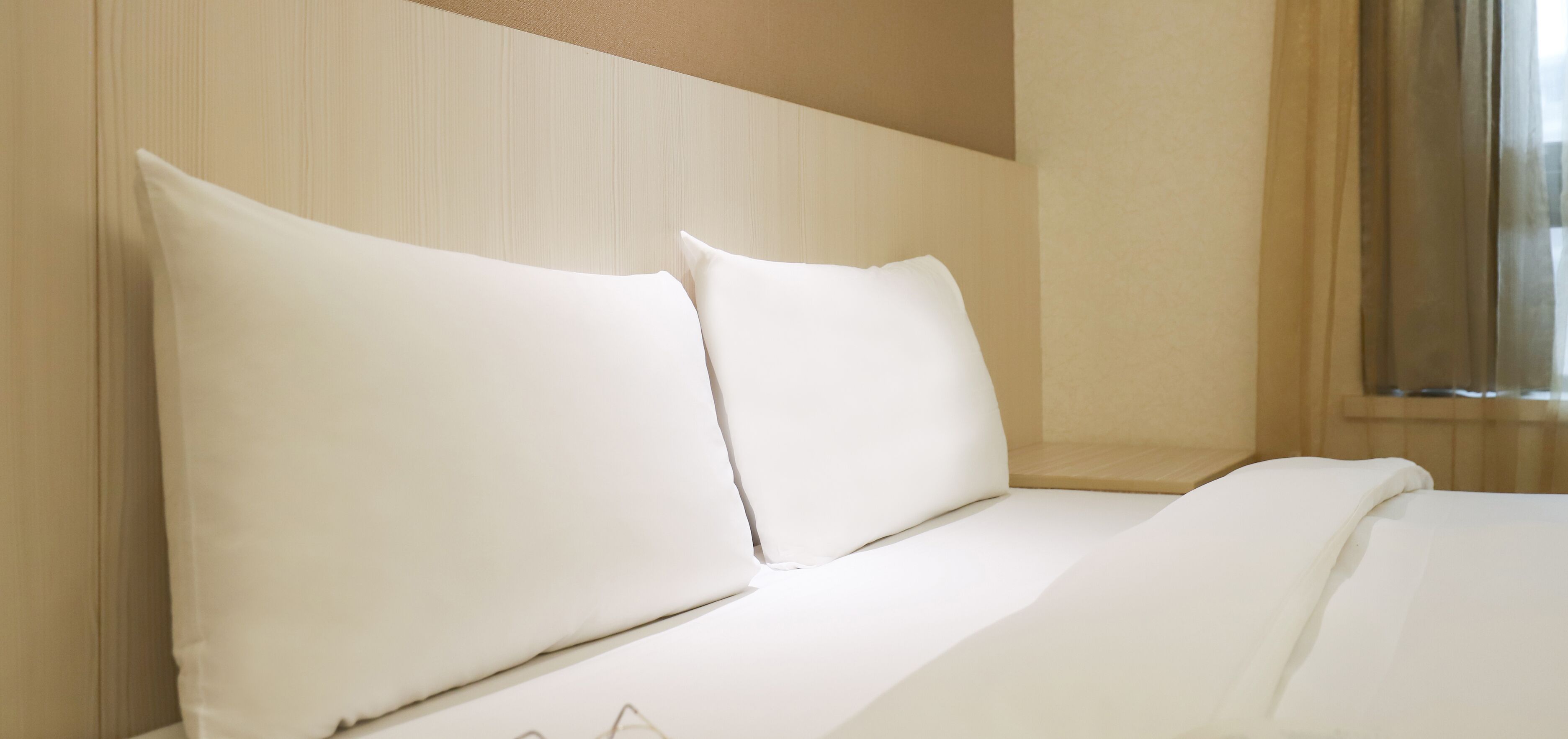 A hotel room with a neatly made bed, a headboard, and a window with curtains.