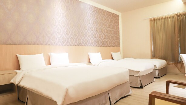A hotel room with two beds, a wooden headboard, a patterned wall, and a large window with curtains. - Anho Chew Hotel (Luodong)