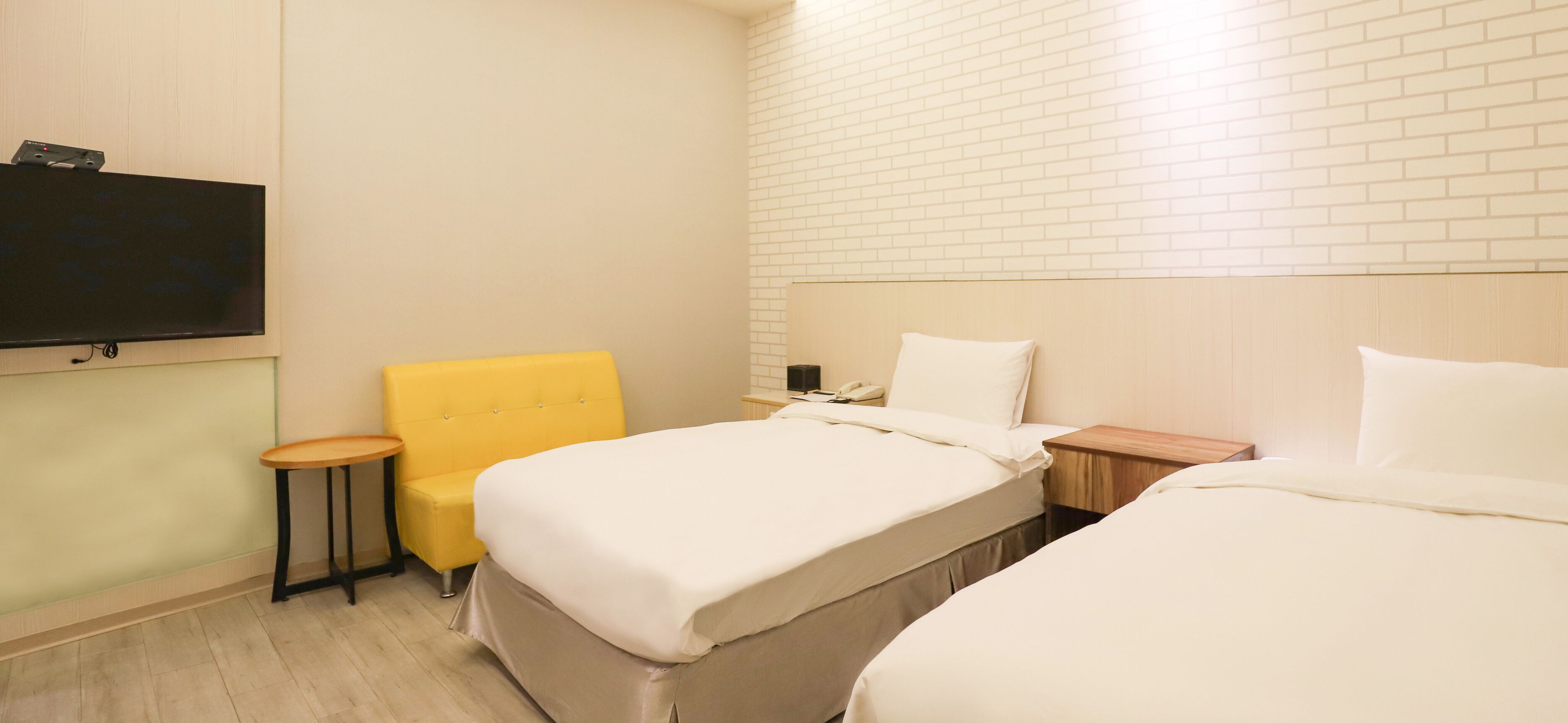 Une chambre d’hôtel avec deux lits, un téléviseur fixé au mur, une petite table et une chaise jaune.