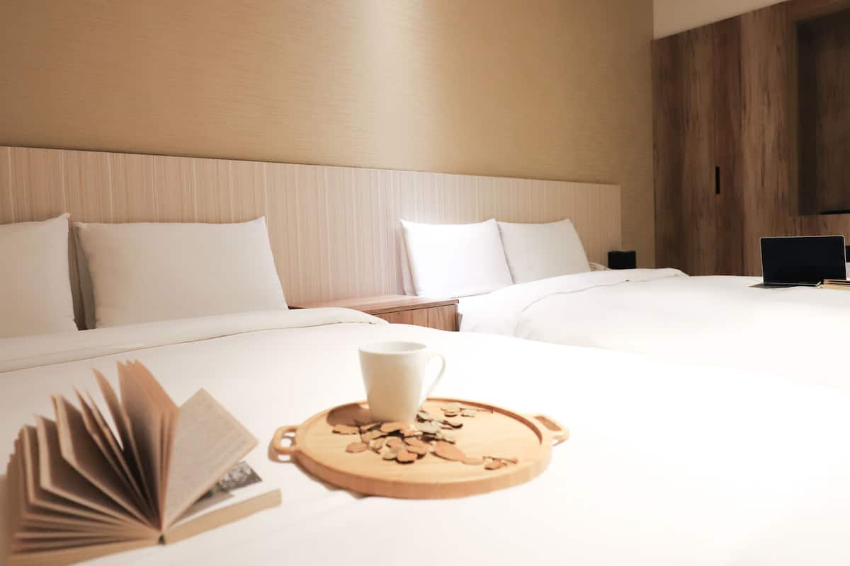 A hotel room with two beds, a wooden headboard, a flat-screen TV, and a tray with a cup and cookies.