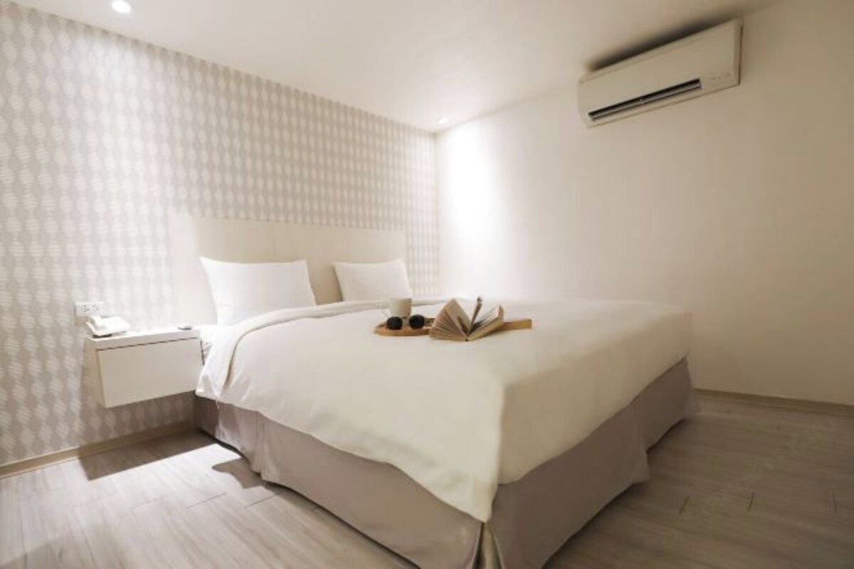 Ein modernes Hotelzimmer mit einem ordentlich bezogenen Bett, einem Nachttisch mit Lampe und einer wandmontierten Klimaanlage.