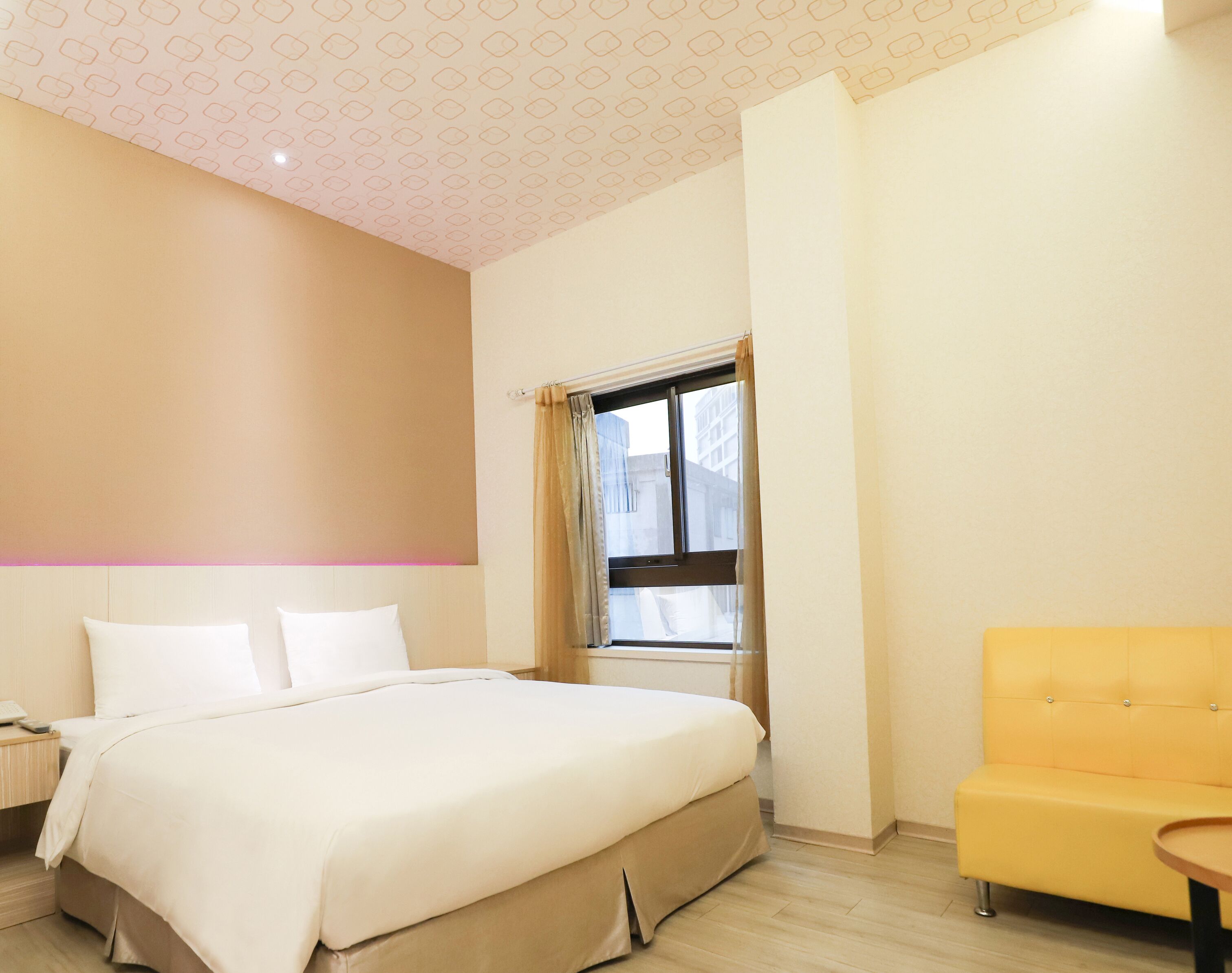 A hotel room with a bed, a window with curtains, a yellow armchair, and a nightstand with a lamp.