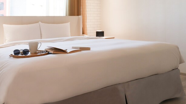 A neatly made bed with a tray of breakfast items, a book, and sunglasses on a hotel room. - Anho Chew Hotel (Luodong)