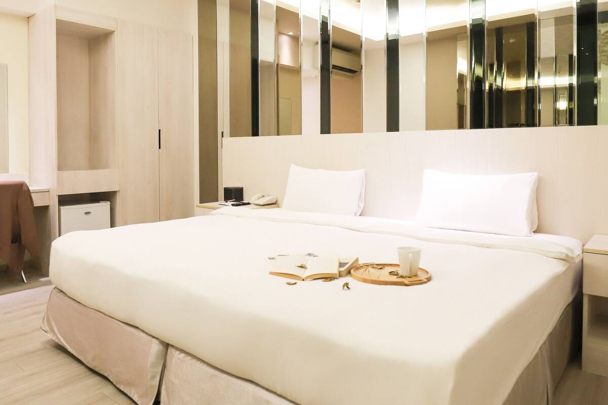 A modern hotel room with a large bed, a desk, and a mirror.