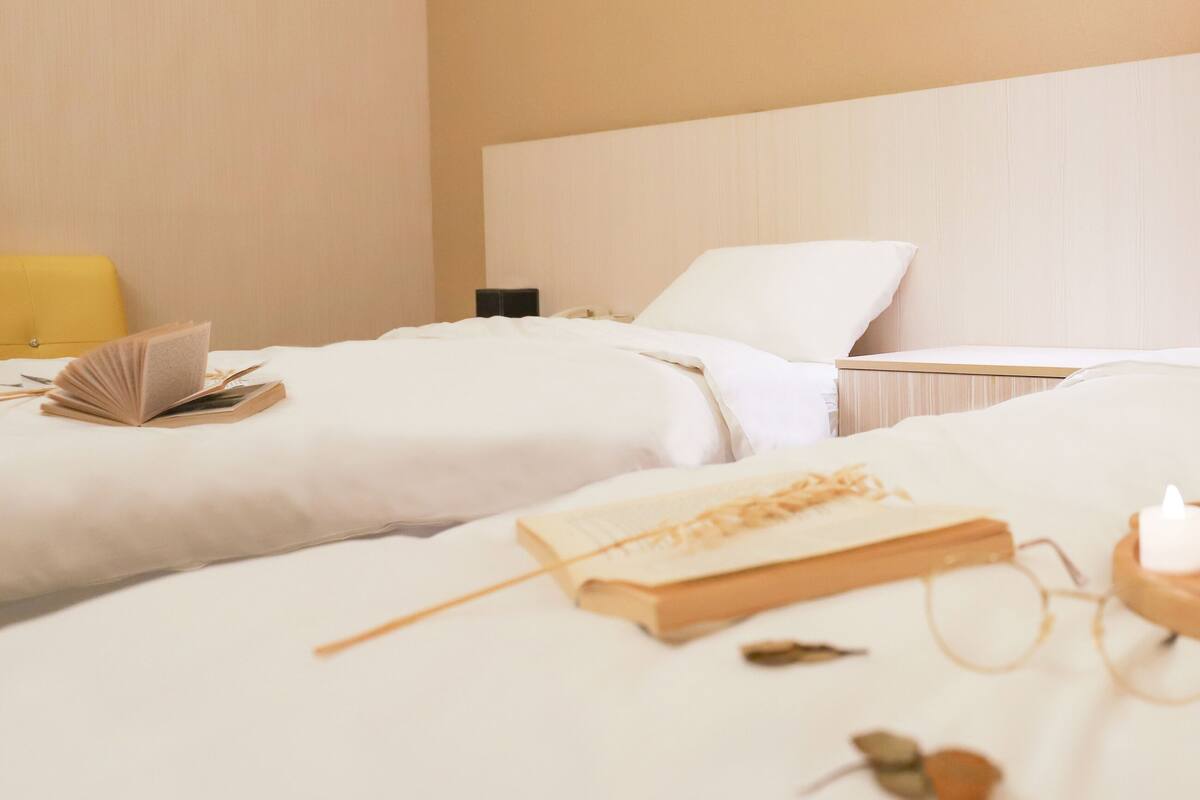 A hotel room with two beds, a bedside table with a book, glasses, and candles.