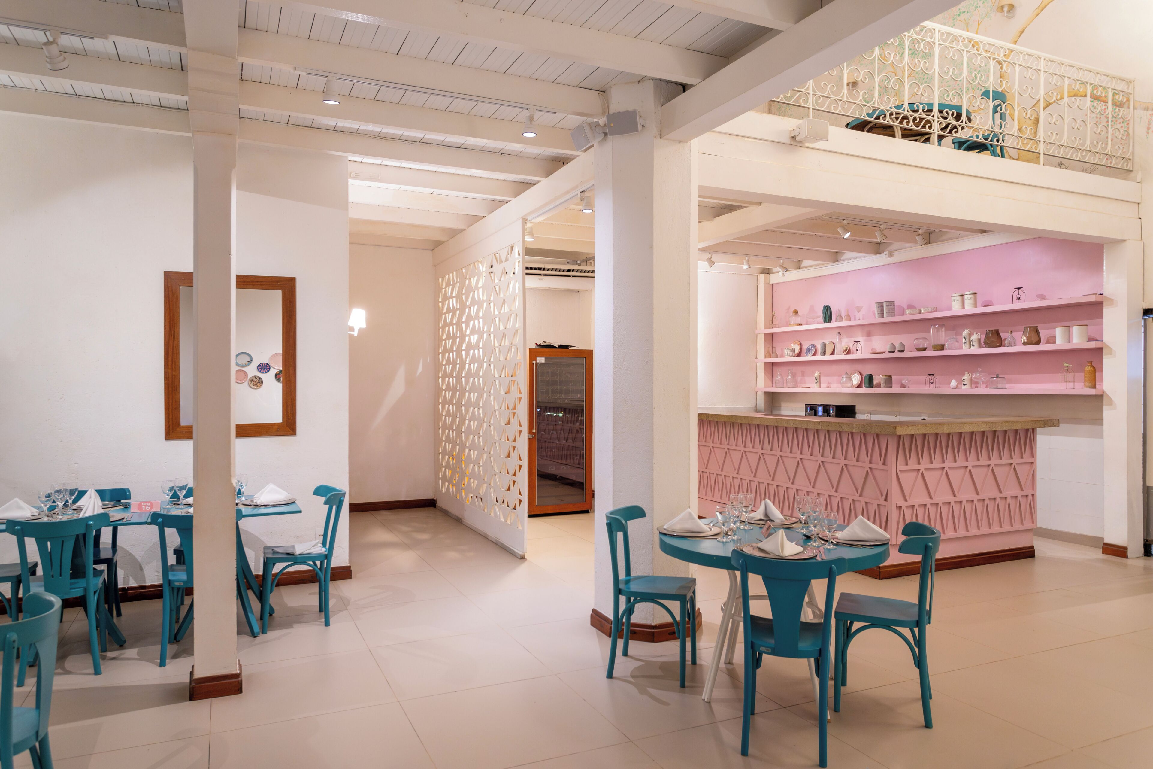 A modern interior with teal chairs and tables, a pink bar area, and a white ceiling with exposed beams.