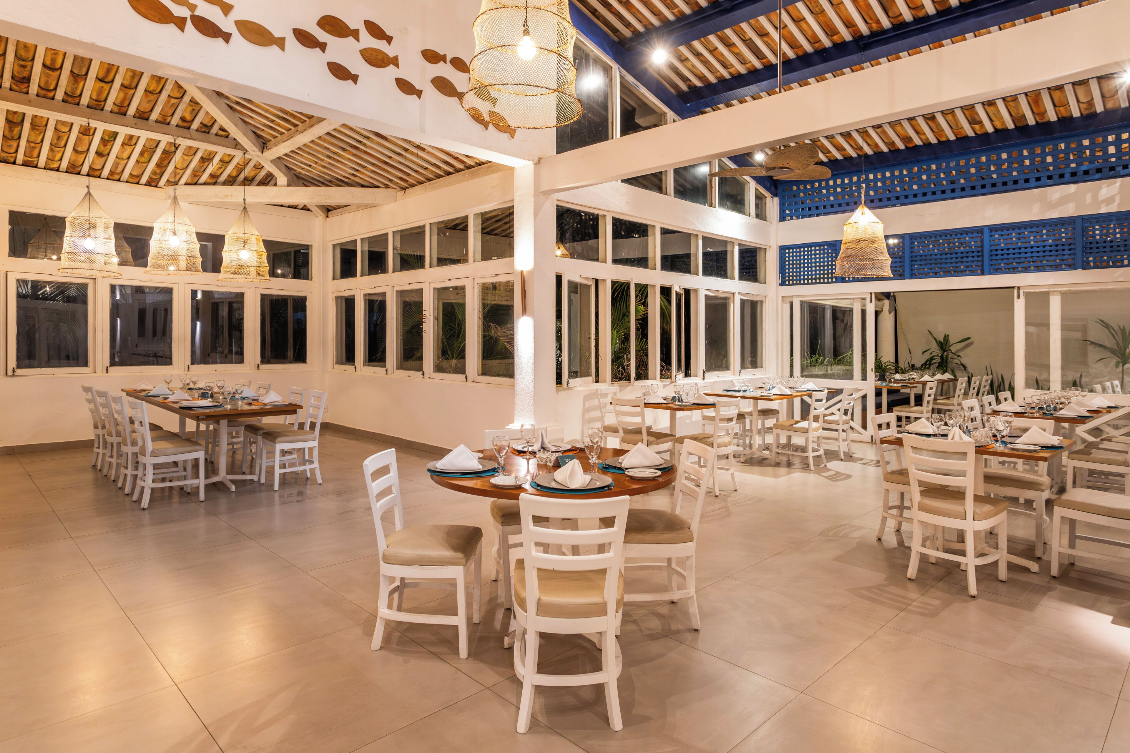 A spacious dining area with multiple tables and chairs, large windows, and hanging pendant lights.