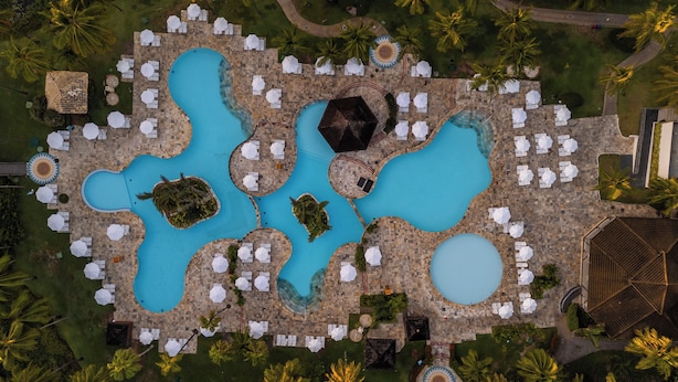 An aerial view of a resort with multiple swimming pools, lounge areas with umbrellas, and palm trees. - Sauipe Terra Resorts - All Inclusive (Mata de São João)