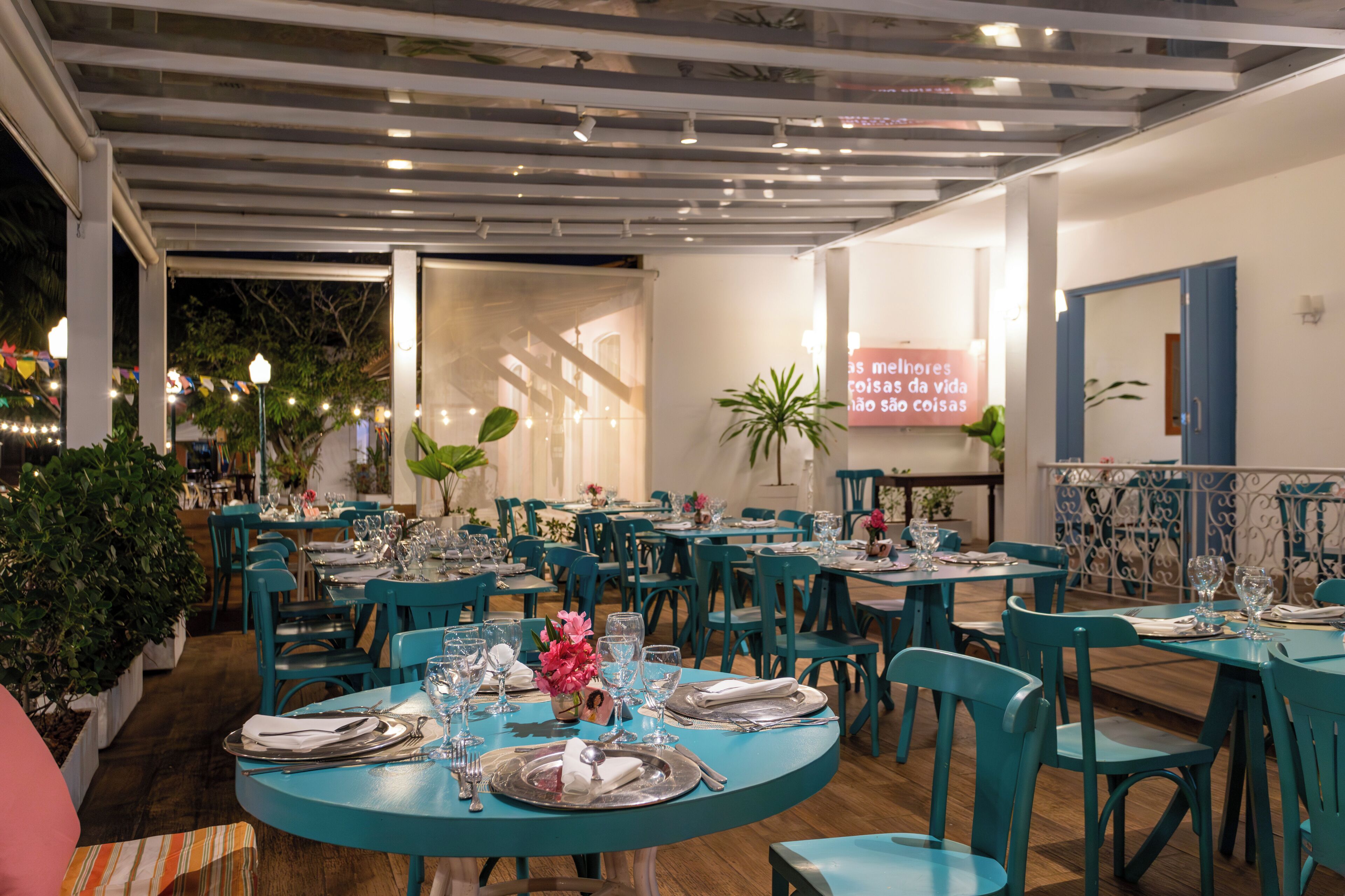 Ein Restaurant mit taubenblauen Tischen und Stühlen, Zimmerpflanzen und einem Projektionsschirm mit Text.