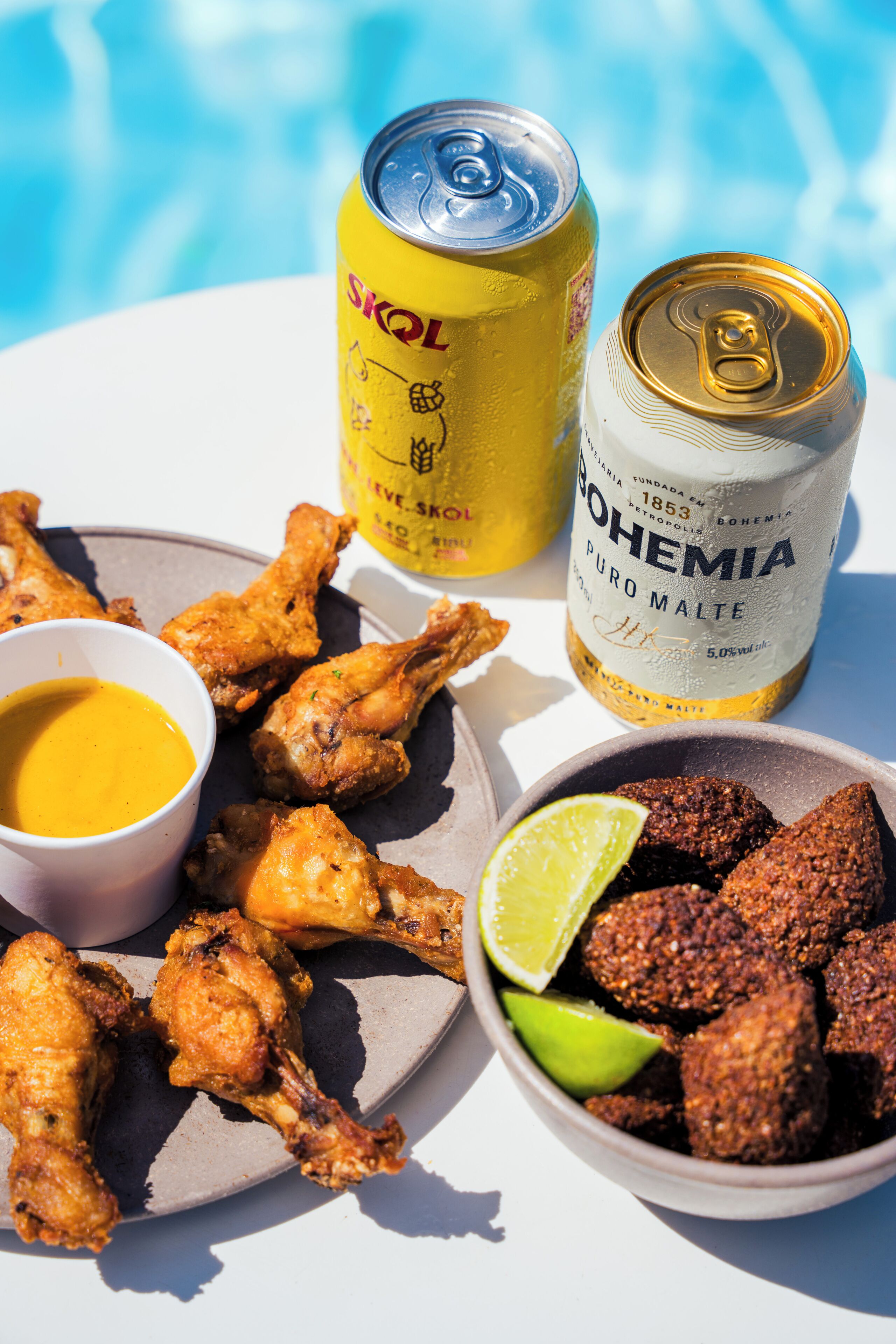 A plate of fried chicken, a can of beer, a bottle of beer, and a bowl of fried snacks.