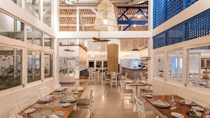 A spacious dining area with multiple tables set for dining, a central bar area, and large windows providing views. - Sauipe Terra Resorts - All Inclusive (Mata de São João)