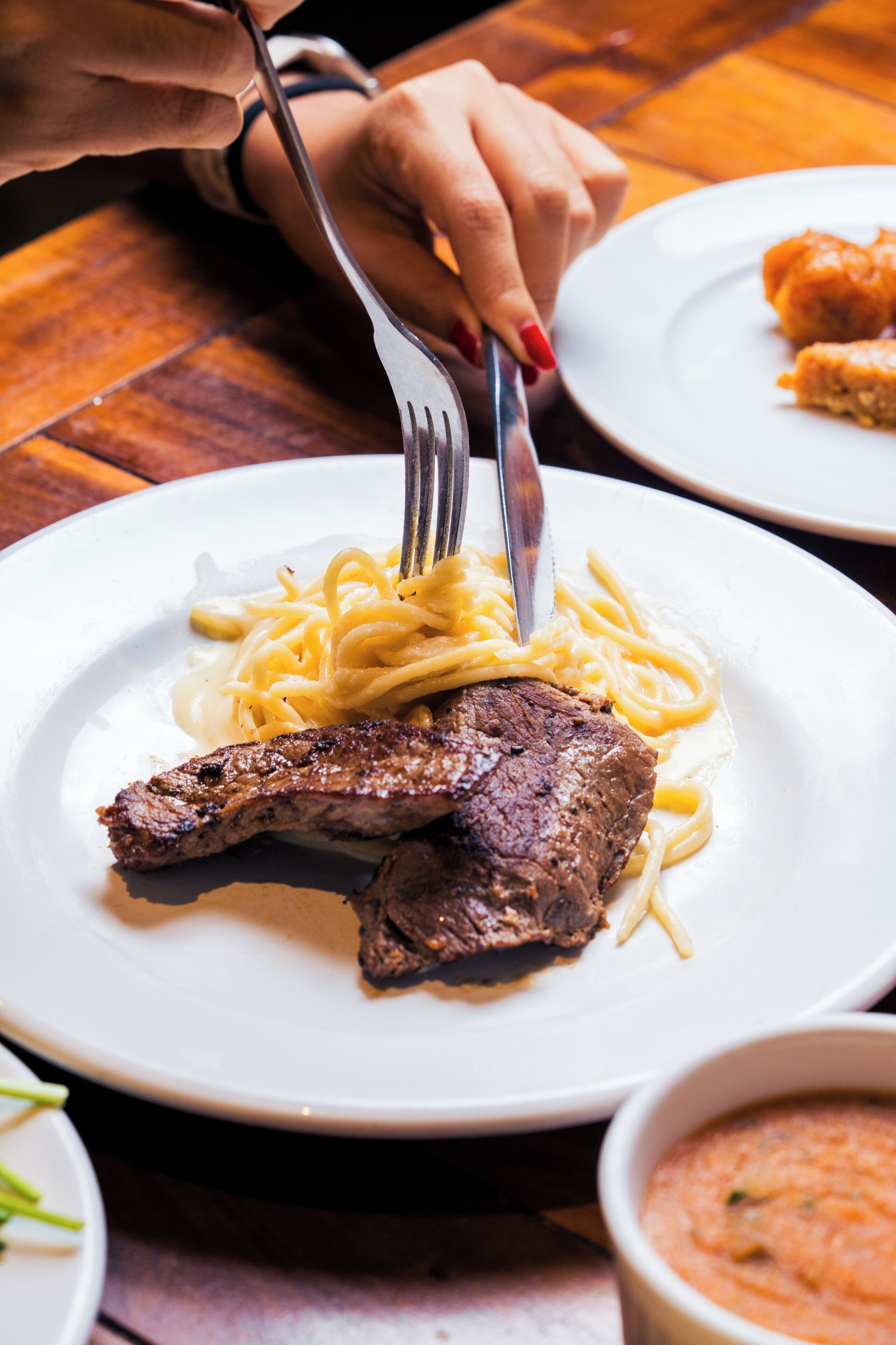 A plate of food with a steak and pasta, a fork, and a knife on a table.