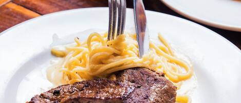 A plate of food with a steak and pasta, a fork, and a knife on a table.