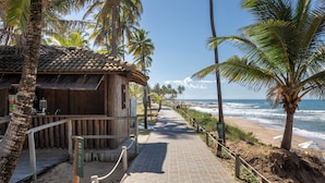 A wooden building with a tiled roof, a paved walkway, and palm trees along a beachside path. - Sauipe Terra Resorts - All Inclusive (Mata de São João)