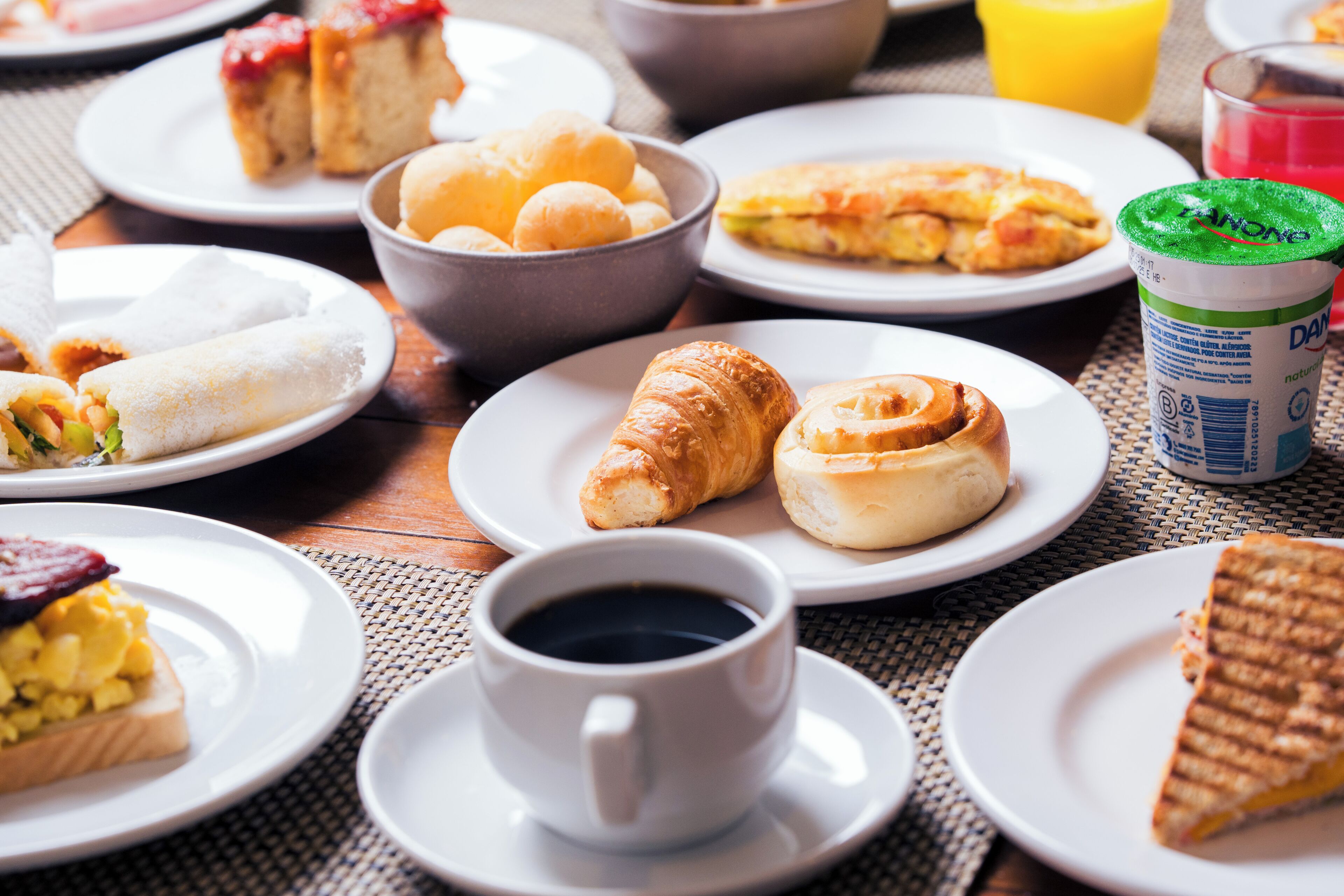 A breakfast setting with various food items on plates, a cup of coffee, and a juice container.
