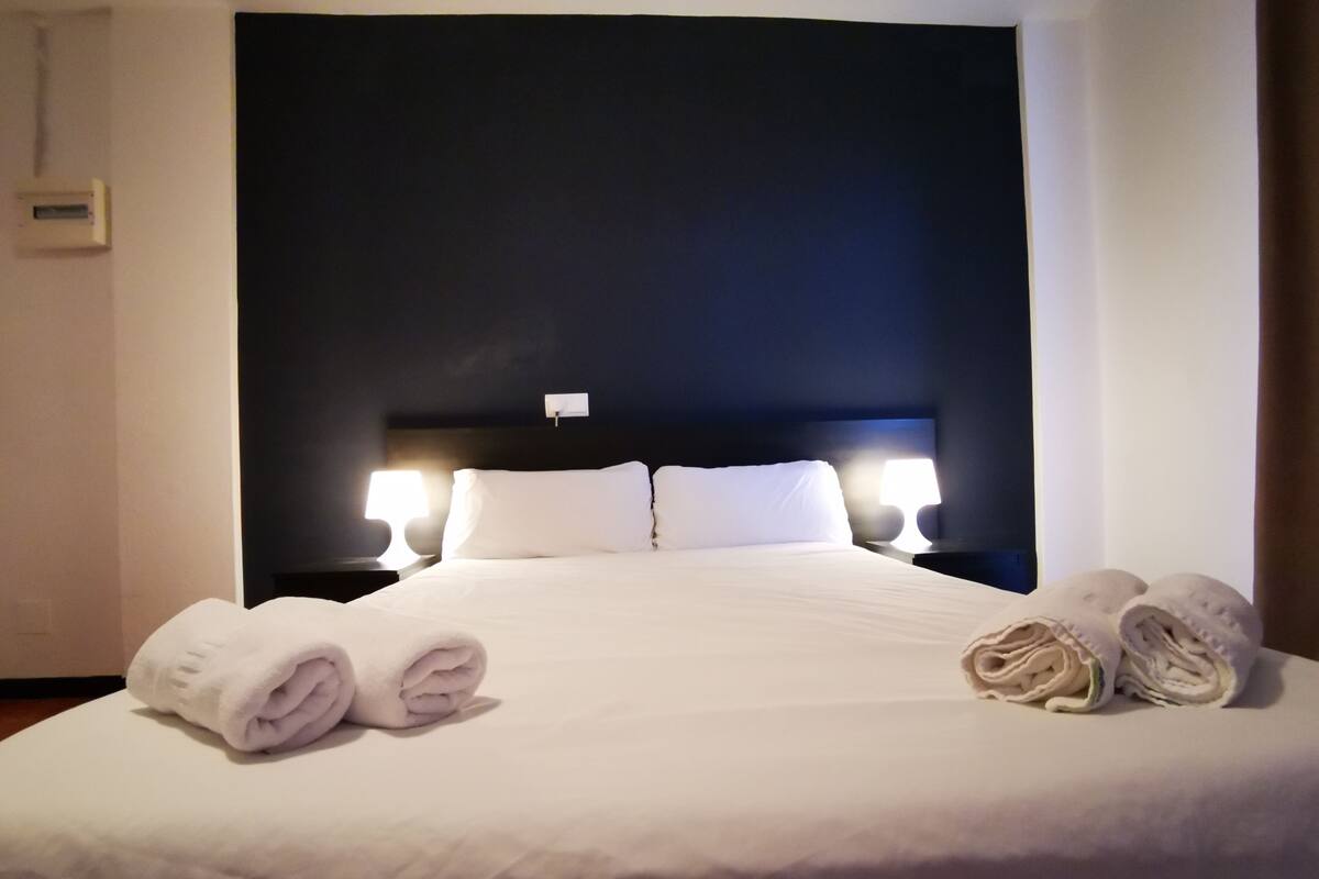 Ein ordentlich bezogenes Bett mit weißen Leinen und zwei aufgerollten Handtüchern an der Seite.