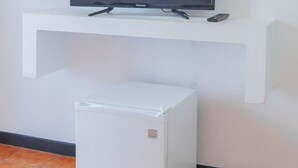 Un téléviseur à écran plat posé sur une étagère blanche, une télécommande et un réfrigérateur blanc en dessous.