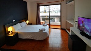 Une chambre d’hôtel équipée d’un lit, d’une télévision, d’un ventilateur de plafond et d’un balcon offrant une vue sur les bâtiments.