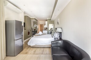 A hotel room with a bed, a black leather sofa, a refrigerator, a lamp, and a television. - The Haystack on Homestead (Sandton)