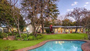 A swimming pool surrounded by a brick border, with a well-maintained lawn and trees. - The Haystack on Homestead (Sandton)