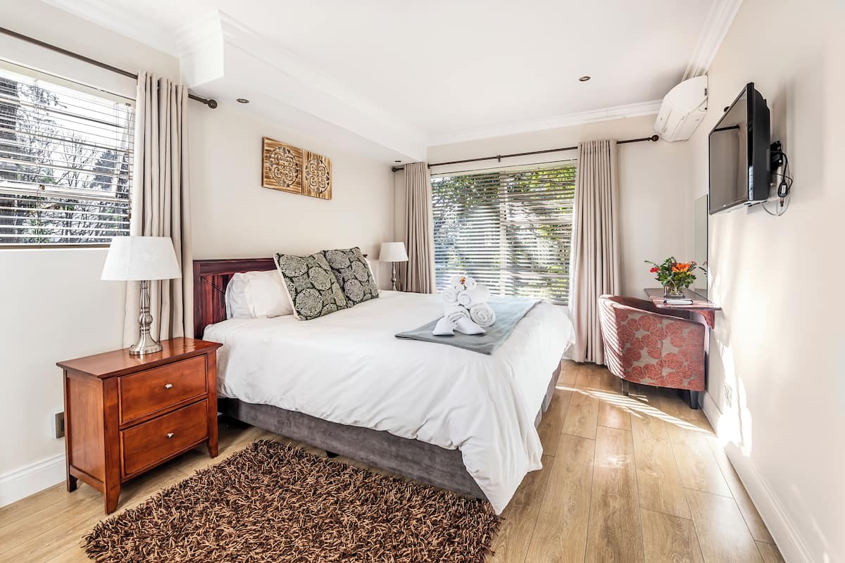 Un dormitorio con cama, mesita de noche, lámpara y una pequeña mesa con un jarrón.