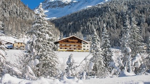 Un albergue de montaña con fachada de madera, rodeado de árboles nevados y montañas.