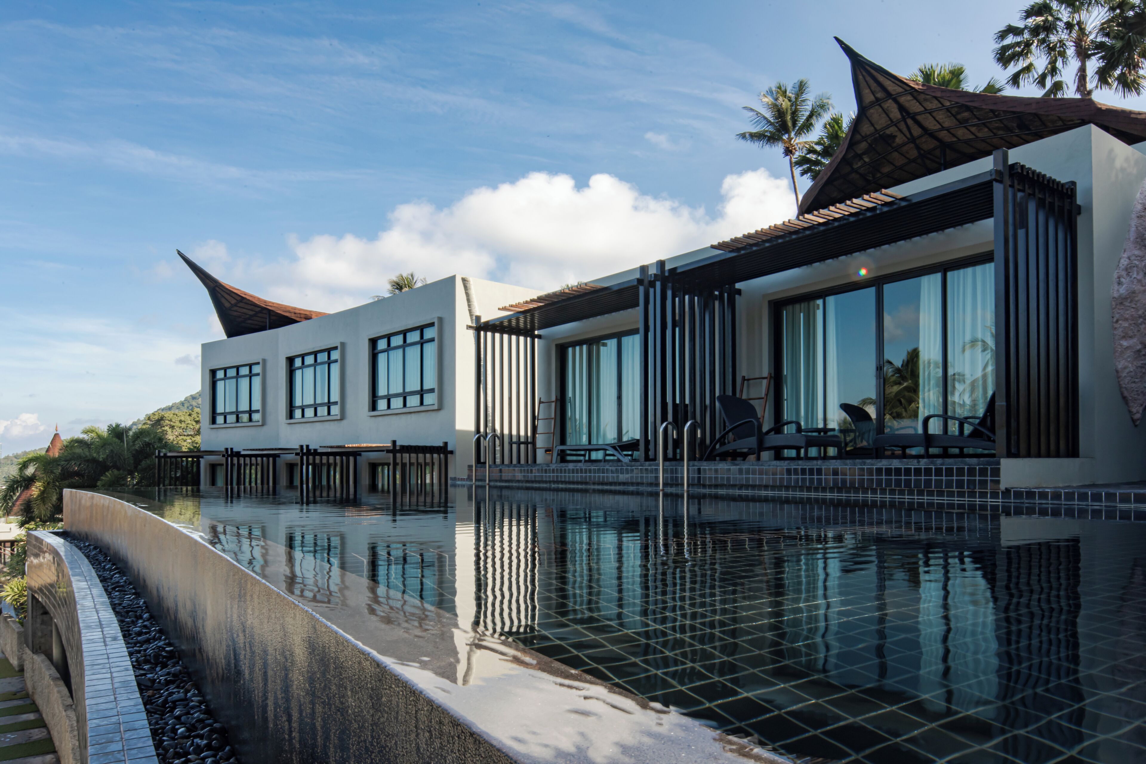 A modern building with a pool, large windows, and a covered seating area.