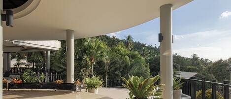 A covered outdoor area with a curved ceiling, potted plants, and a view of a forested hill.