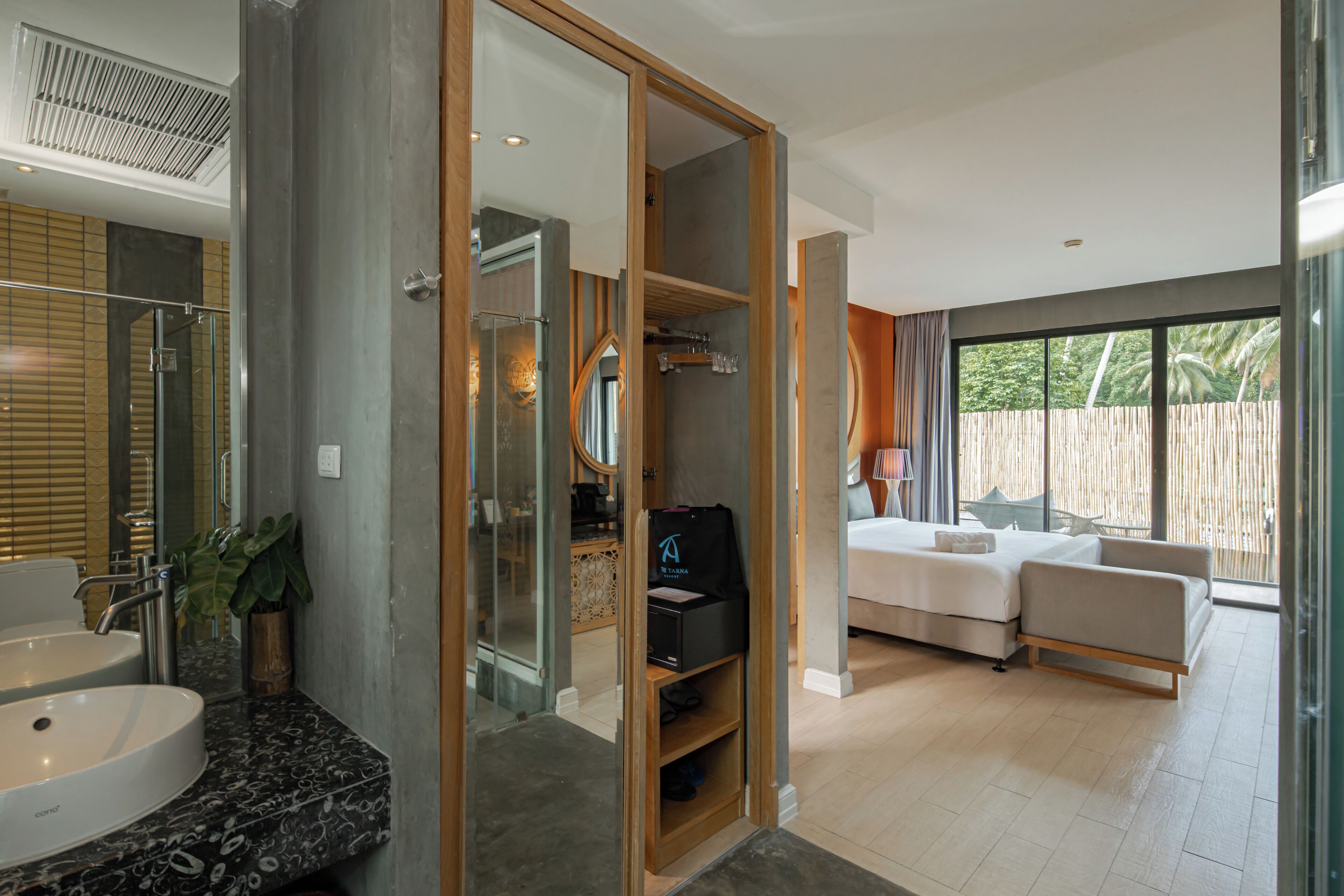 A modern hotel room with a large bed, a bathroom with a sink and mirror, and a balcony with a view of the outdoors.