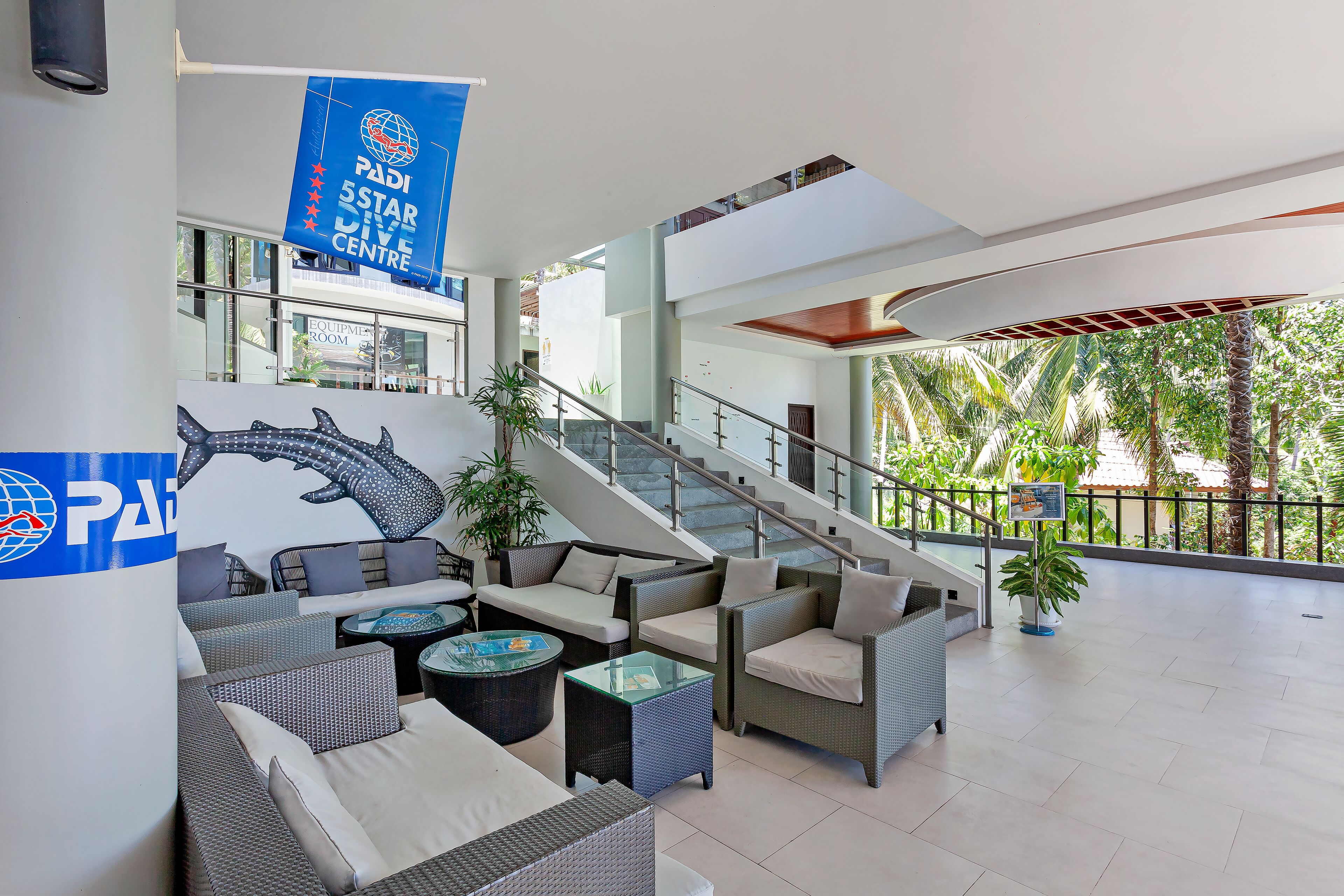 A spacious lobby with a modern design, featuring a staircase, comfortable seating areas, and a view of the outdoors.