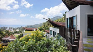 A modern building with large windows, a sloped roof, and a view of a lush landscape with trees and a distant view of the sea. - The Tarna Resort, Koh Tao (Koh Tao)