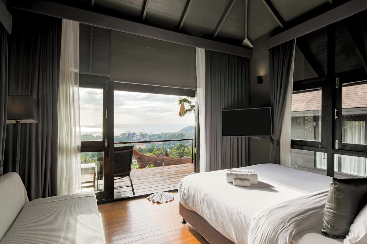 A hotel room with a balcony, a bed, a chair, and a TV.